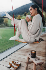 Frau sitzt auf einer Schaukel auf einer Terrasse , hält eine Tasse Tee in der Hand und genießt die Düfte der Natur und ihres Tees.