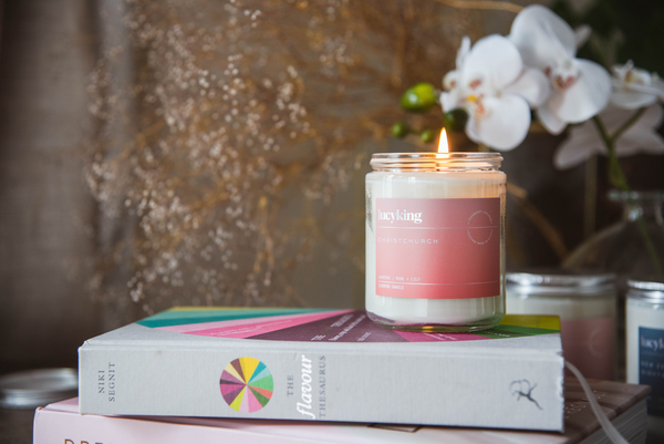 LucyKing CHRISTCHURCH Candle with lit wick placed on top of stack of colourful books