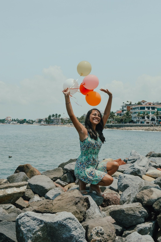 Woman sitting while holding balloons near the sea
