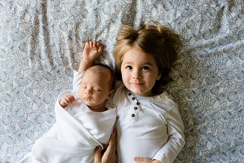 Baby and young child laying on a bed