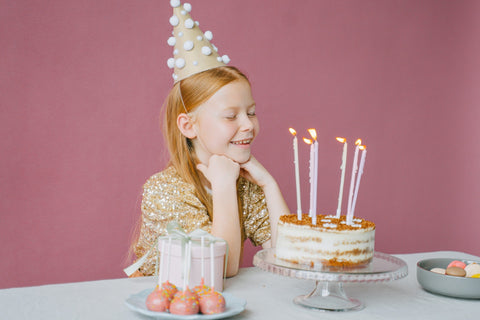 A young girl is making a wish sitting at a table in front of a birthday cake 