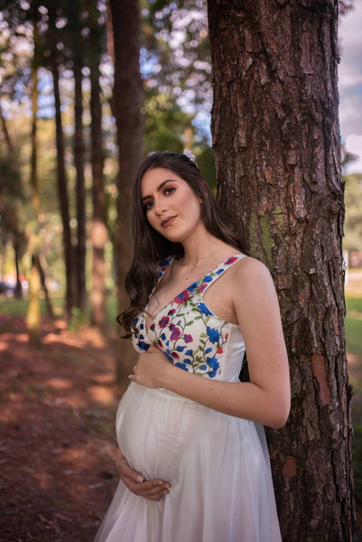 Pregnant lady wearing a floral maternity dress standing against a tree
