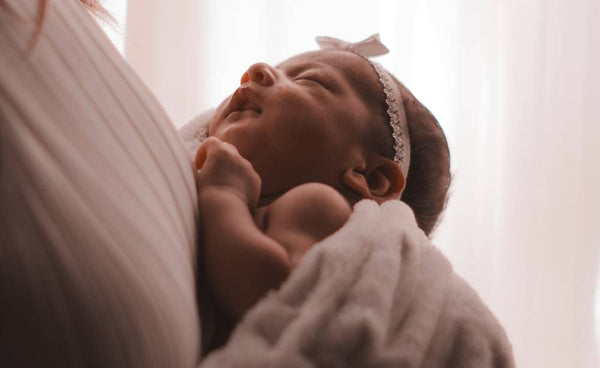 A newborn baby girl wearing a pink headband with bow is asleep in her mother's arms