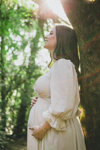 pregnant woman in a white dress leaning against a tree