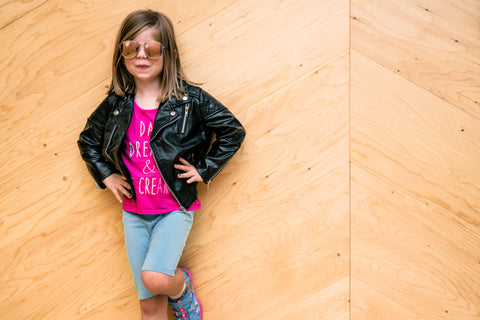 An older girl wearing a pink t-shirt black leather jacket, blue jeans and sunglasses