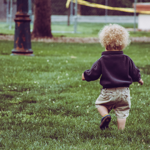 a toddler boy with blond curly hair walks through grass