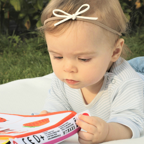 A baby girl lies on her front on a playmat, wearing a bow in her hair