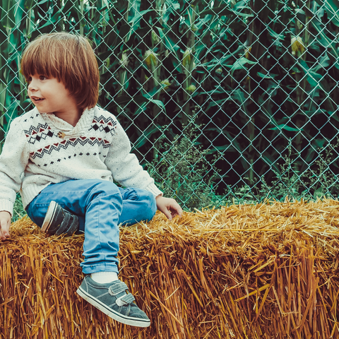 A pre-school boy sitting on a hay stack