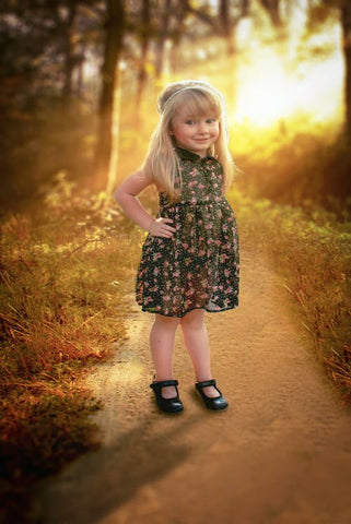 A young girl wearing a pretty floral dress stands on a pathway outside