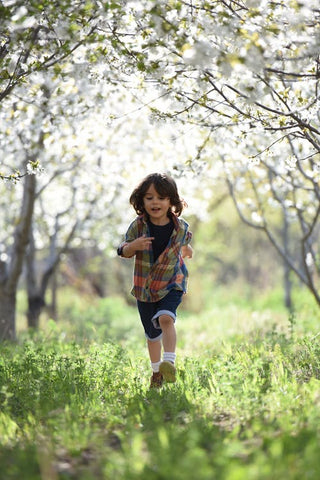 Younger boy walks through a meadow with trees filled with blossom