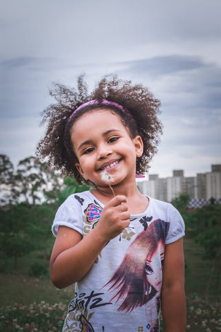 a young black girl smiles for the camera holding a dandelion