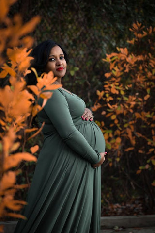 Pregnant woman wearing a green dress surrounded by trees