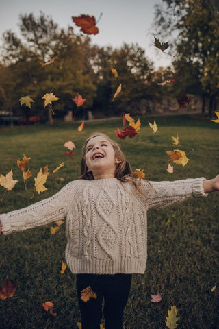 A girl wearing a beige jumper throws autumn leaves up into the air