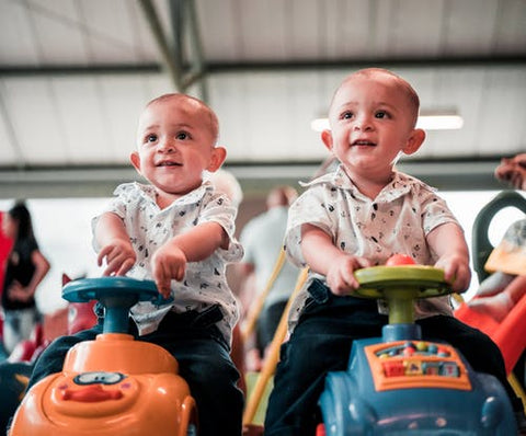 Twin Boys wearing identical outfits sit on toy cars