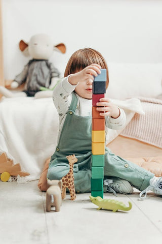 A young child in gender neutral clothes stacks a tower of blocks