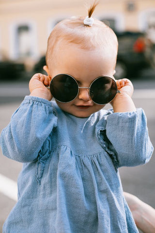 Fashionable toddler girl wearing a denim dress and holding sunglasses over her eyes