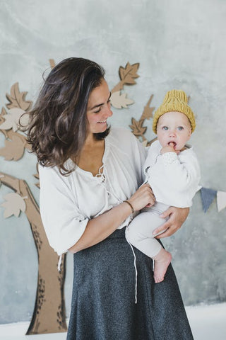 A woman carries a toddler child wearing unisex children's clothes and a knitted yellow hat