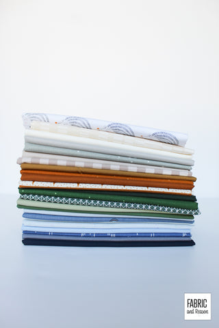 24 fat quarters of quilting cotton in blue, green, burnt orange, and neutral tones, folded and  stacked vertically in front of a white surface.