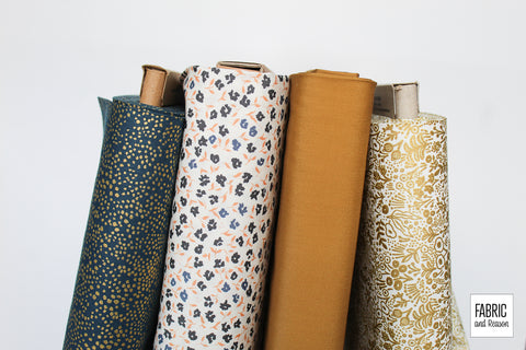 4 bolts of fabric stacked vertically. Prints include little navy flowers, navy with gold dots, and golden flowers on a cream background. Solid bolt of leather colored fabric.