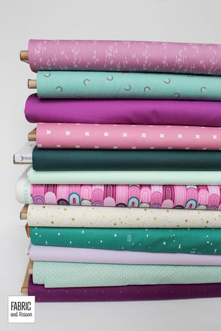 Stack of 12 bolts of fabric laid horizontally in shades of purple and teal with metallic accents.