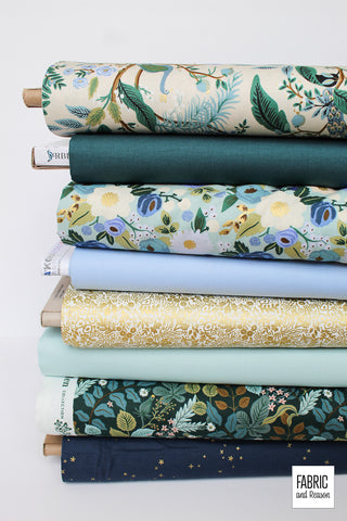 Stack of 8 bolts of fabric laid horizontally in shades of deep teal, cream, gold metallic, and blue.