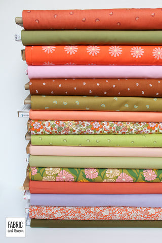 Stack of 16 bolts of fabric laid on their sides. Floral prints are combined with little rainbows and solids in bright oranges and greens with lavender, pink and peach accents.