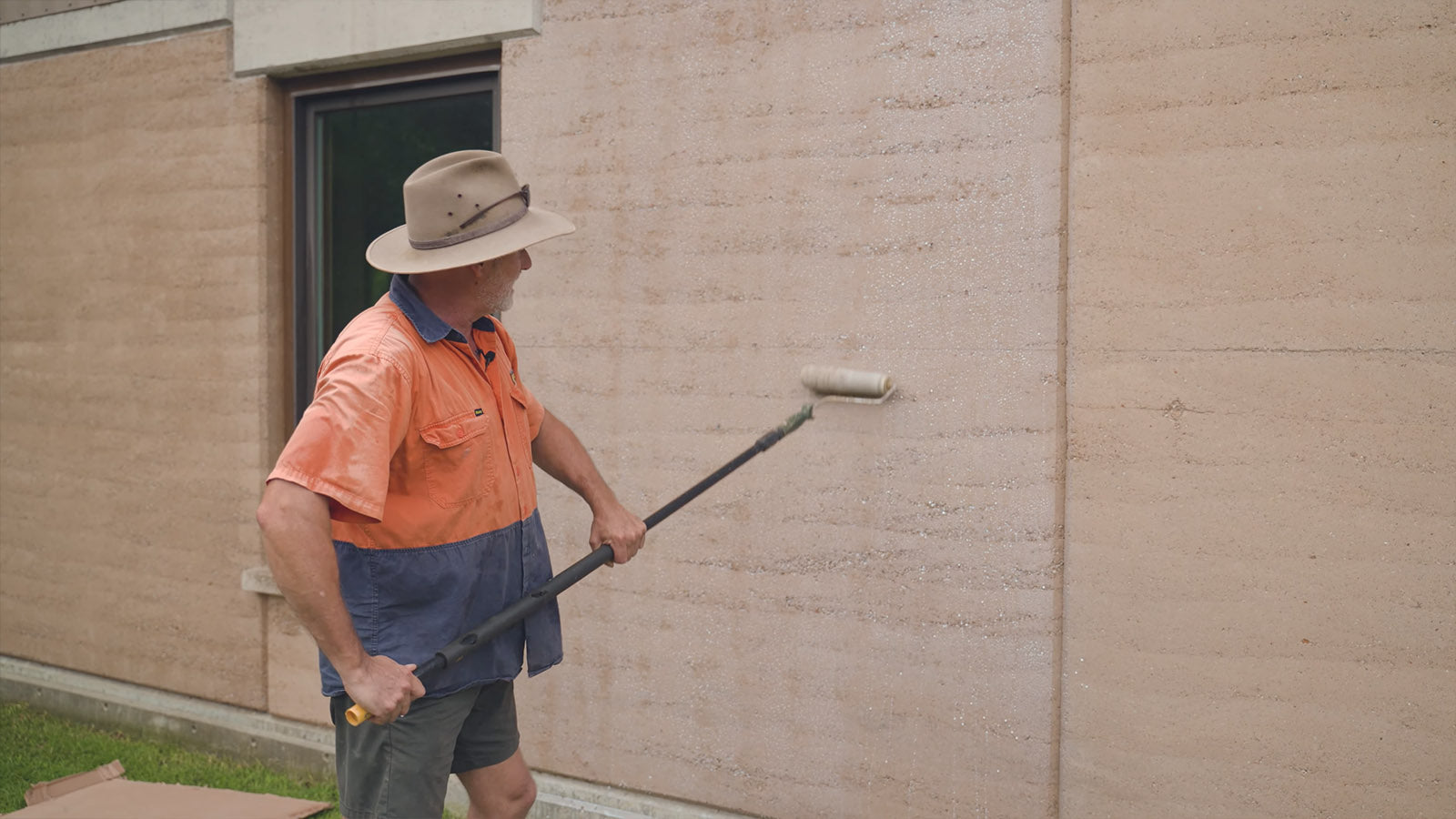 Photo of man applying Earth Binder sealant to rammed earth wall