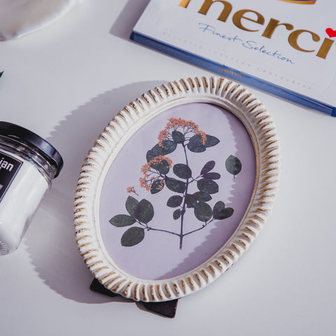 An oval picture frame with Merci dessert on top and a scented candle on the left.