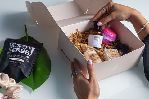 A woman's hands are shown inspecting the white gift box's contents. It mostly contains beauty and skin-care products.