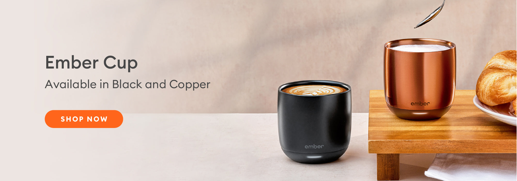 Two Ember Cups in black and copper on a countertop with a croissant sitting nearby.