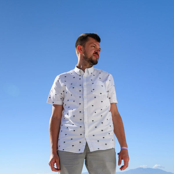 man standing wearing a palm tree pattern button-down shirt with gray chinos by the water.