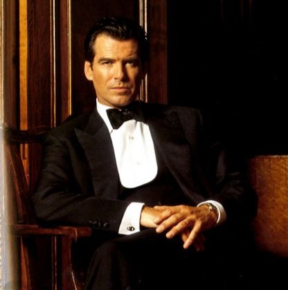 Pierce Brosnanas James Bond Posing oon a wooden chair wearing a black tuxedo