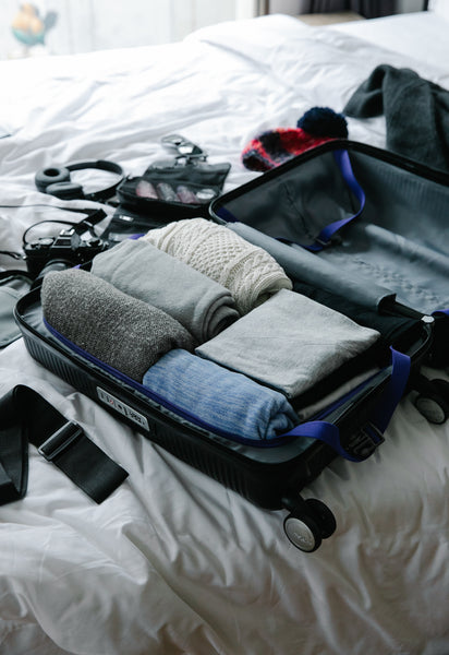 Suitcase on bed packed with folded clothes and accessories for travel.