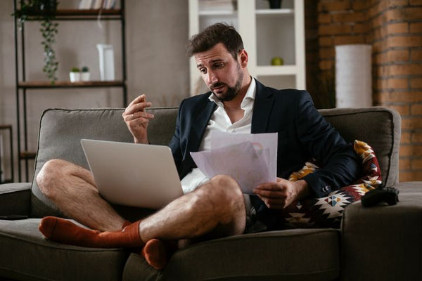 Man sitting on a couch in a navy suit and white dress shirt, underwear and dress socks.