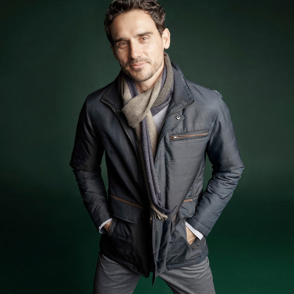 Man posing in a scarf, jacket, and pants against a solid green background