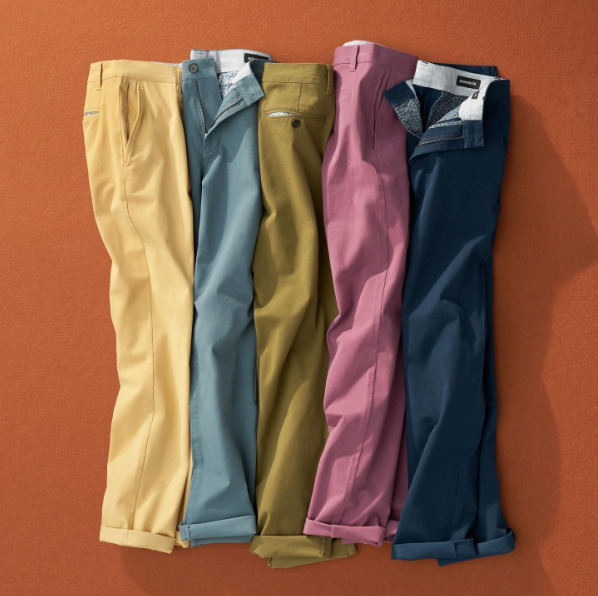 Vibrant-colored pairs of chinos laid out on an orange background.