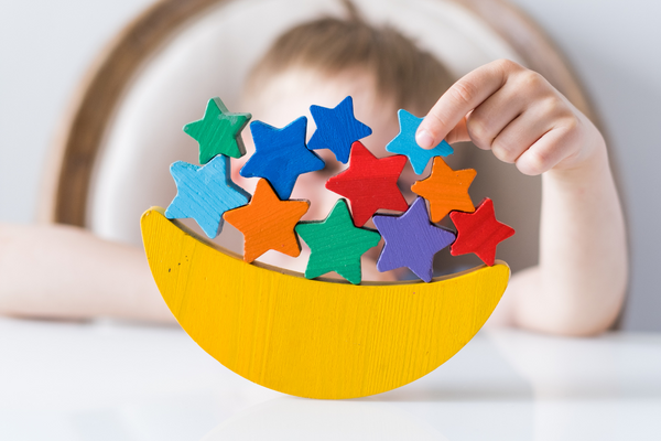 A child's balancing game. The base of the toy is a half moon and the child is trying to balance colorful stars on the base.
