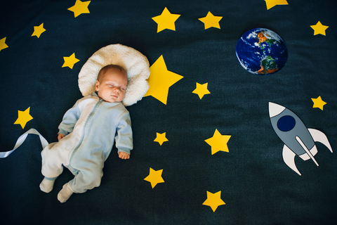 A baby sleeping on a blanket. The blanket has yellow stars of different sizes, a spaceship and earth.