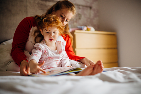 A mother and daughter reading a book in a child's room.