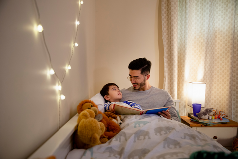 A father and son sitting in a child's bed reading a story.