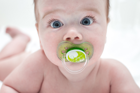 Baby lying on stomach with green pacifier in mouth