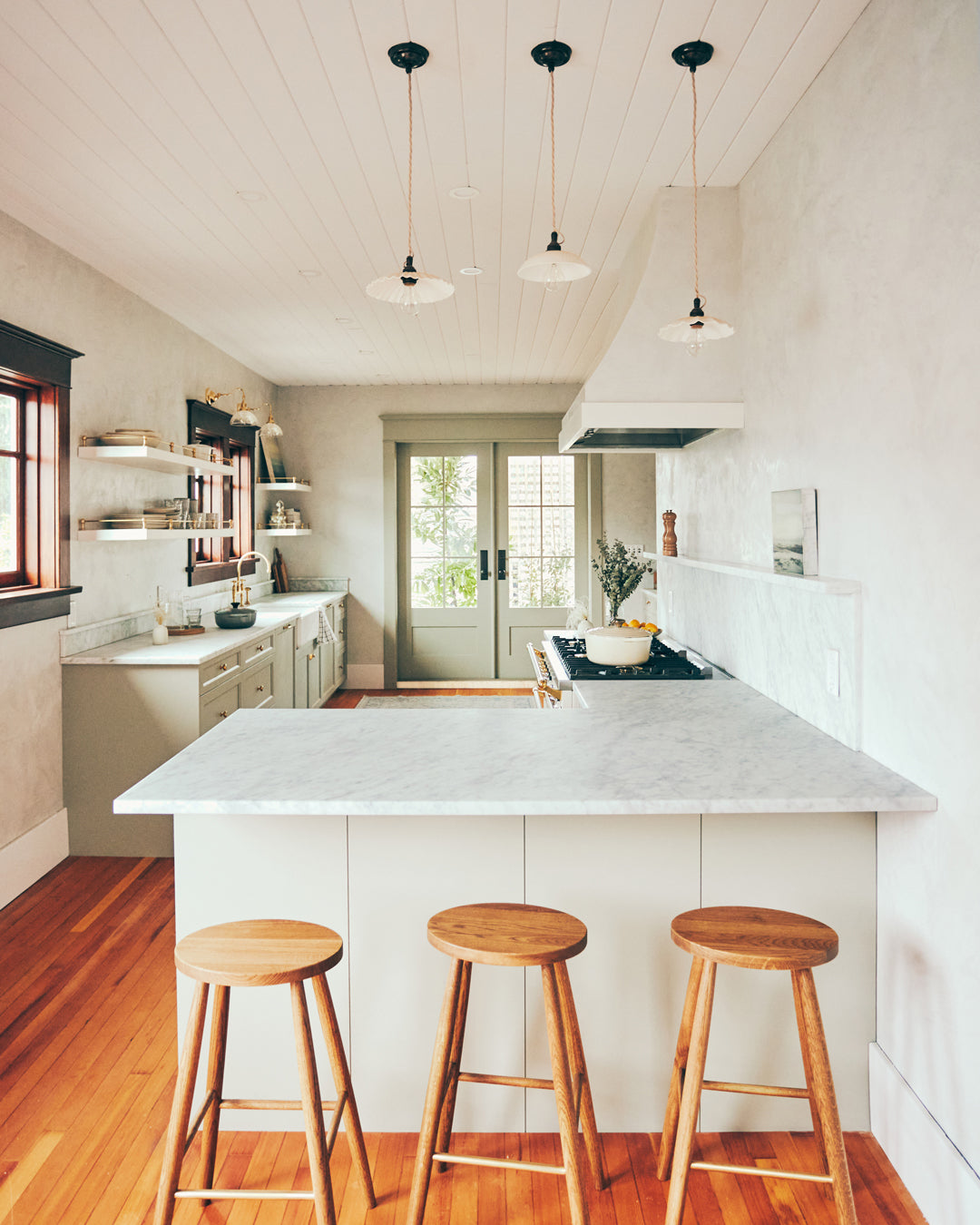 White kitchen with bar stools in front and french doors leading to the back yard in the background. The doors have Grandeur Fifth Avenue Knob in Timeless Bronze on them.