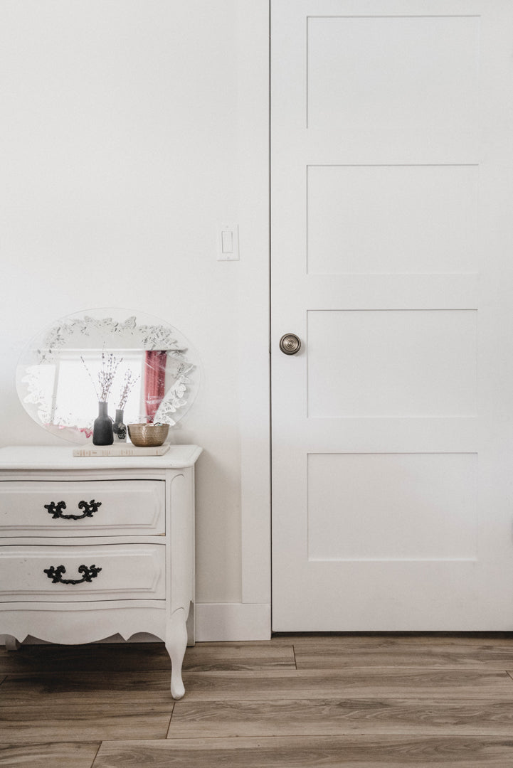 White door with a Soleil Rosette with Soleil Knob in Satin Nickel closed with a white side table next to it.