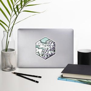 A hexagonal sticker with a snowy mountainscape illustration is attached to a laptop.