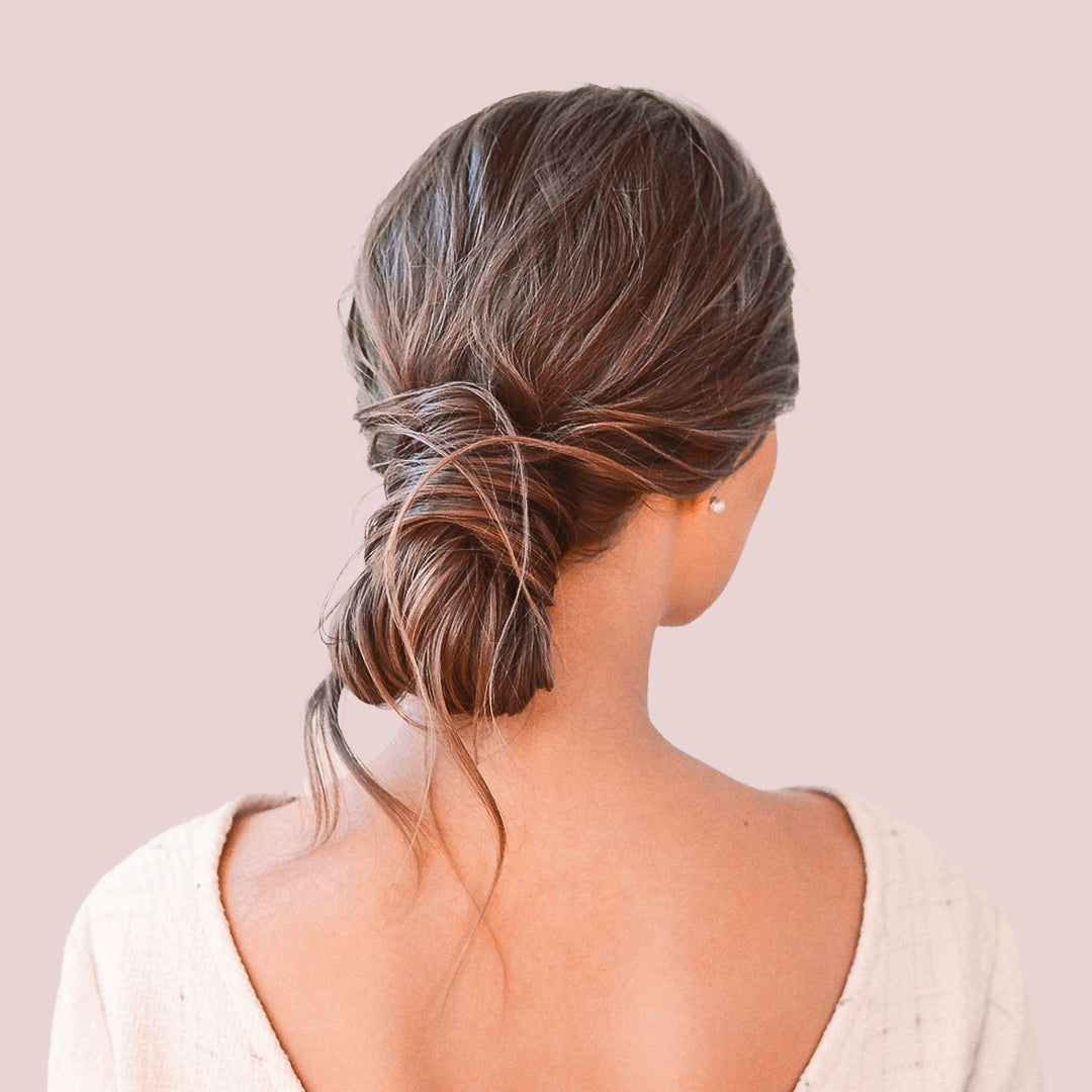 Back view of a woman with her hair styled in a tousled chignon wearing a cream sleeved blouse