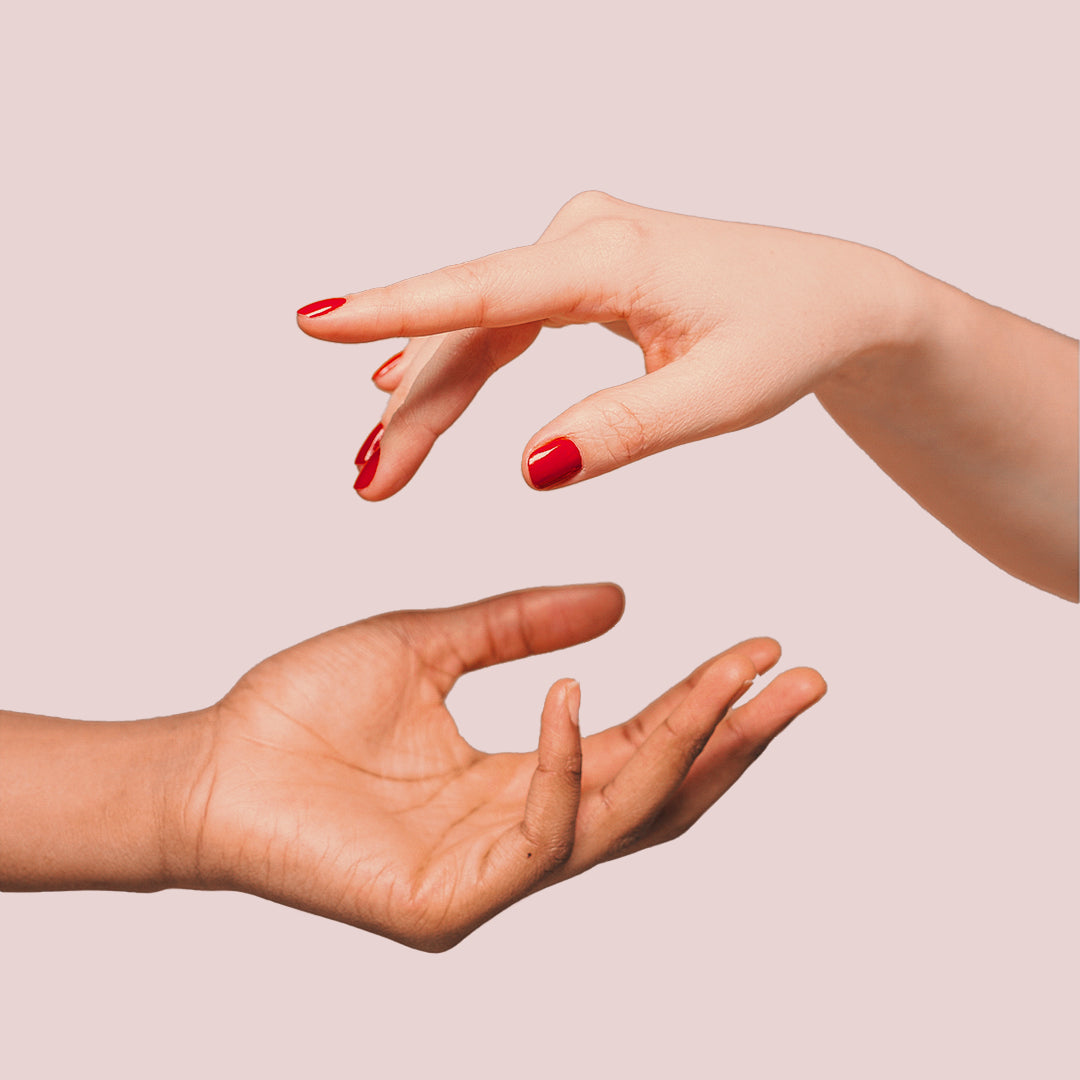 A pair of hands with red painted fingernails reaching out to each other