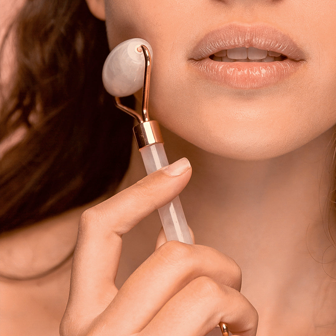 A woman wearing lip gloss holding a jade roller to her cheek