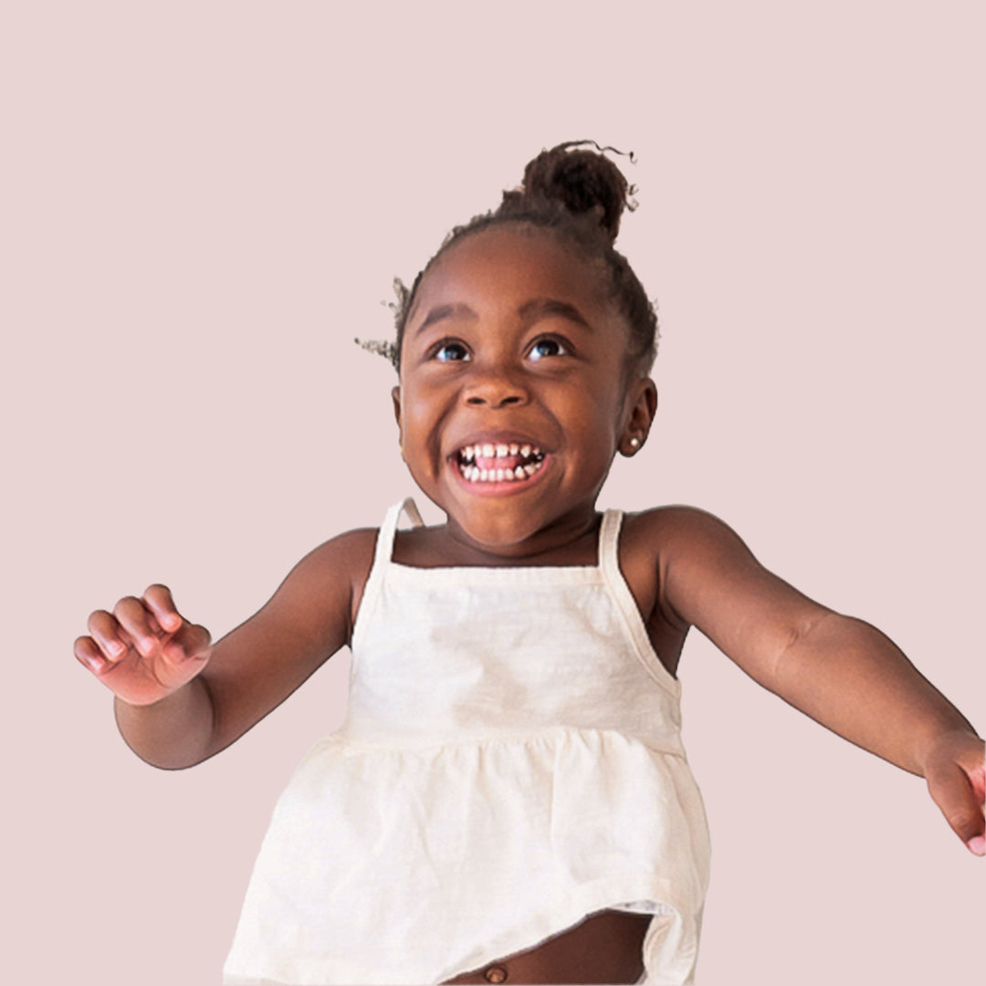 A smiling child wearing a white tank top mid jump with her arms out