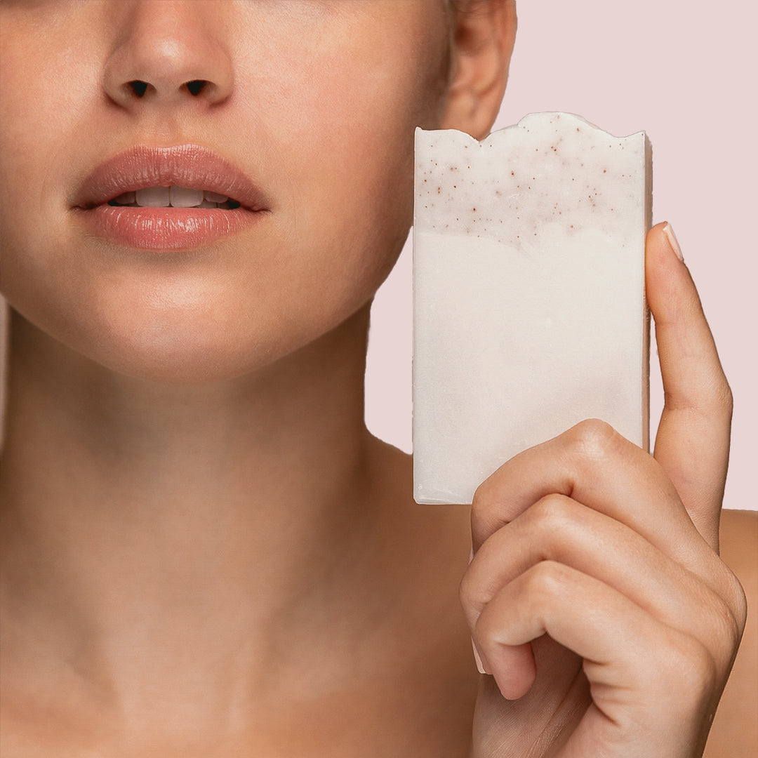 Close up of a woman's face while she is holding up a bar of soap for facial
