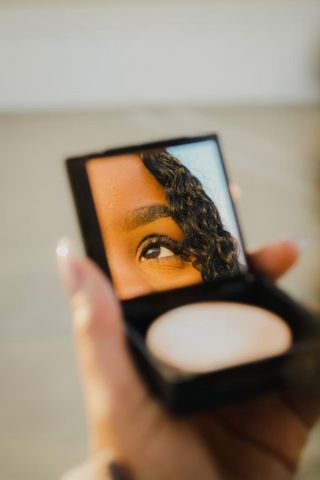Compact mirror with a reflection of an eye against a beige backdrop